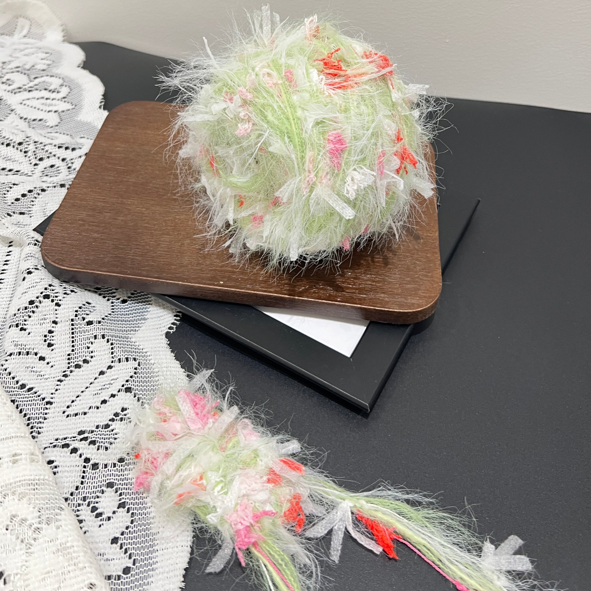 Front overhead spherical shot soft pastel lime base hand-blended yarn ball mixed with blush pink & coral red petal ribbon fiber accents, airy layered fuzzy texture