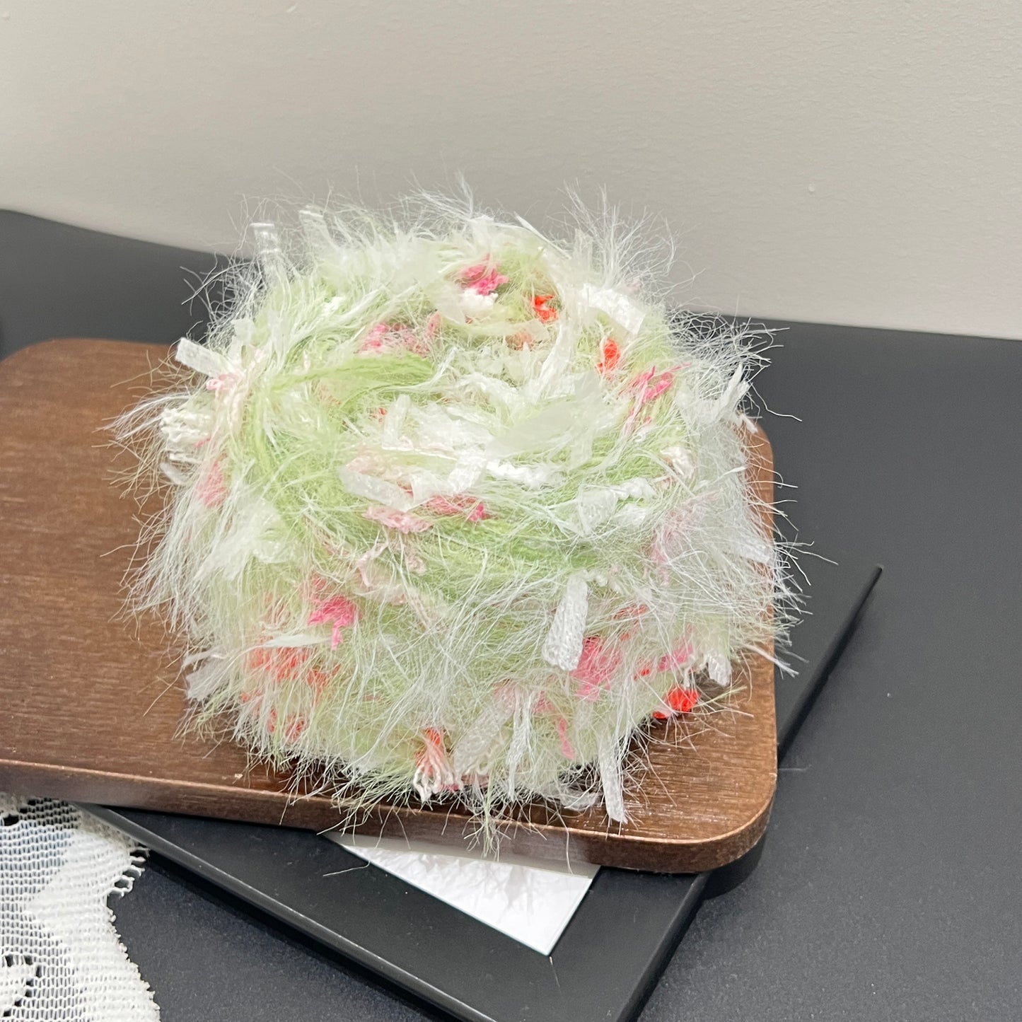 Complete display set: lime floral yarn cake + matching long-tassel fiber swatch beside perforated white lace fabric on dark matte countertop
