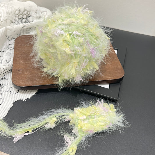 Pastel lime yellow lilac floral multi-strand hand-blended cake yarn placed on wooden board with white lace backdrop