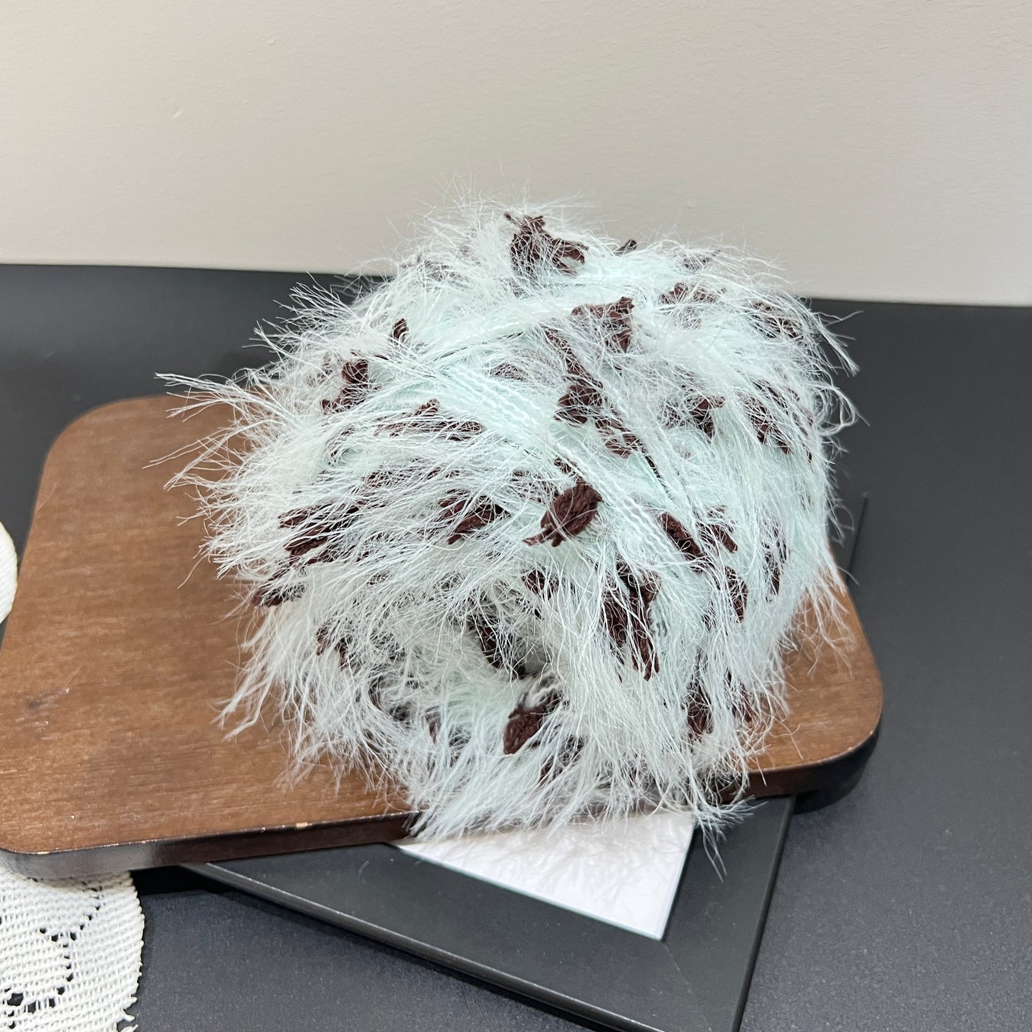 Full display layout of mint brown yarn cake and matching fiber swatch beside hollow lace fabric on dark countertop