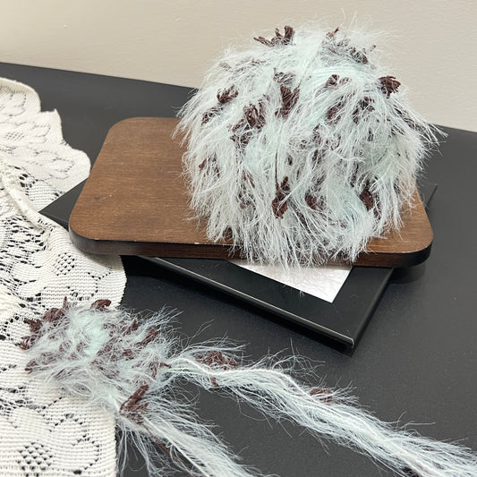 Pastel mint brown floral multi-strand hand-blended cake yarn placed on wooden board with white lace fabric backdrop