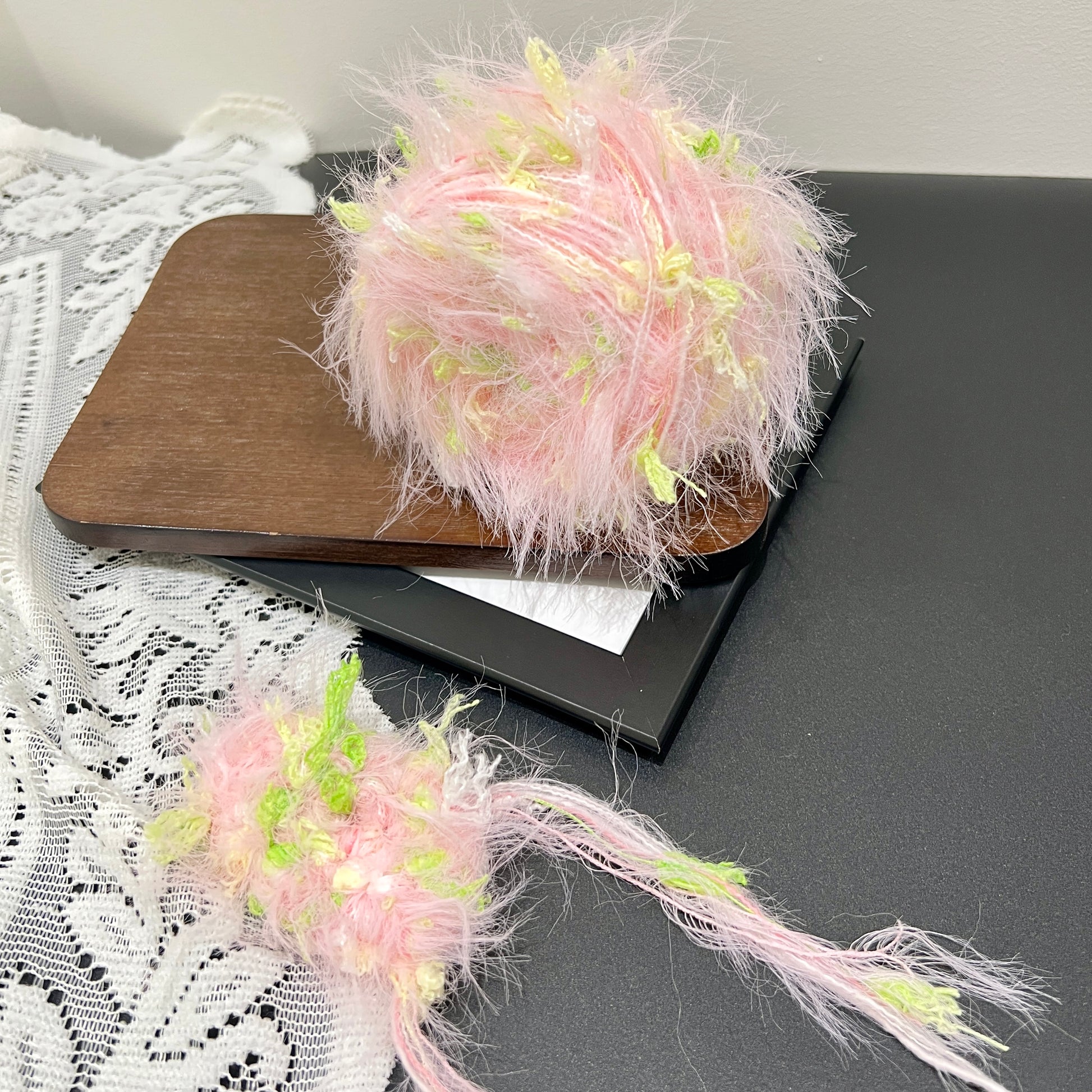 Pastel pink lime floral multi-strand hand-blended cake yarn placed on wooden board with white lace fabric backdrop