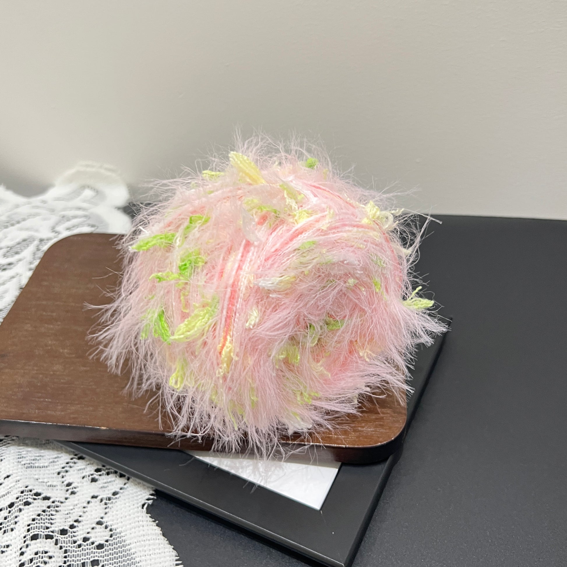 Side angle shot pastel pink lime floral multi-strand blended yarn cake with lime petal fiber accents