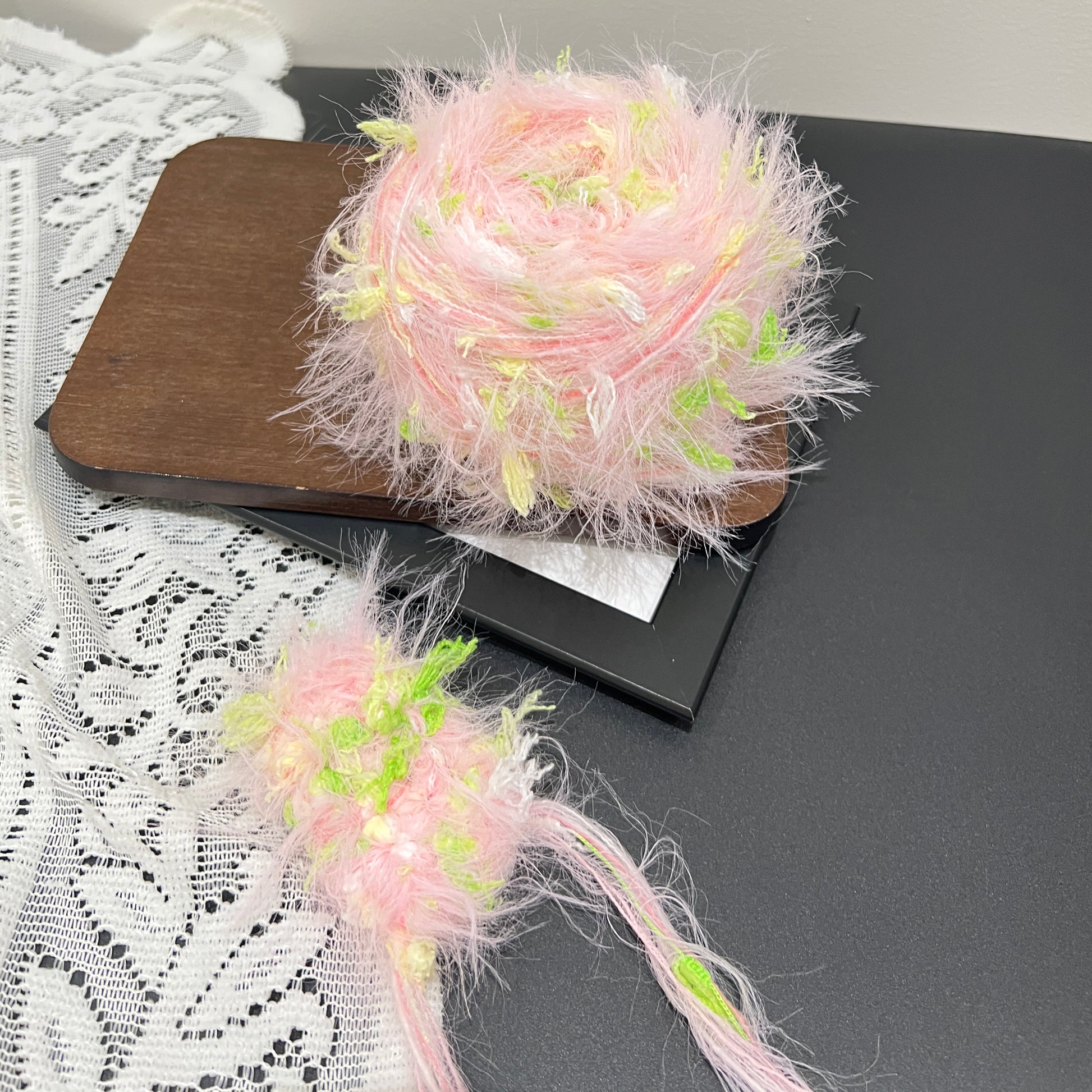 Side layout pastel pink lime floral artisan blend yarn cake and fiber sample swatch on dark countertop