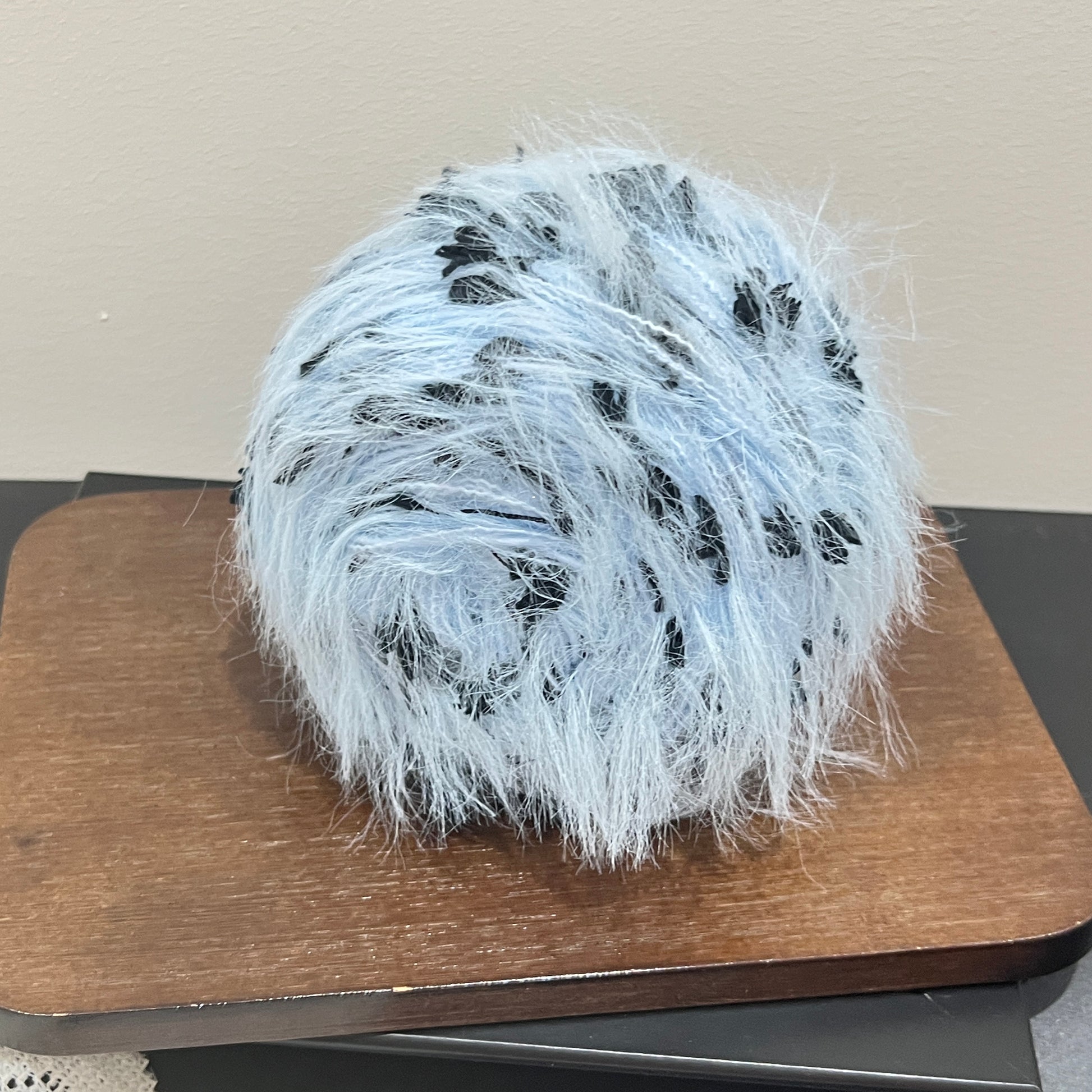Wide layout shot yarn cake + long tassel fiber swatch, perforated white lace fabric laid flat on dark tabletop