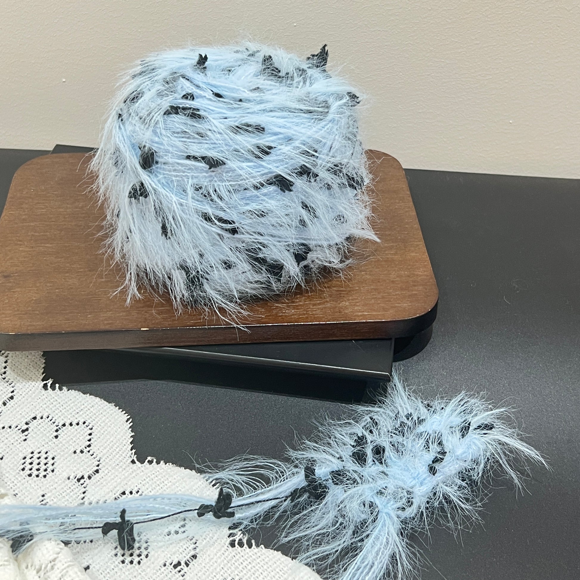 Full layout display set: sky blue yarn ball + detached fiber swatch, hollow white lace fabric on left side, dark matte countertop surface