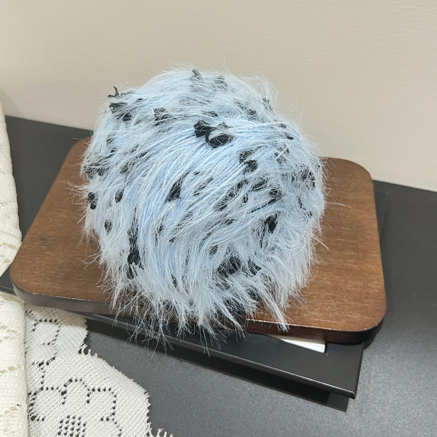 Rotated side overhead shot sky black art yarn cake, multi-color contrast feather and petal fiber clearly visible