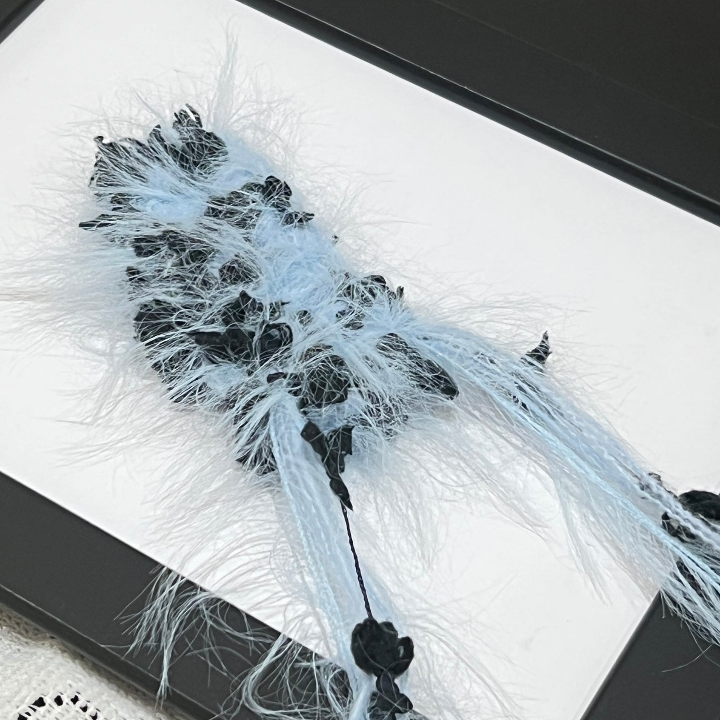 Top-down full round overhead shot sky blue black floral yarn ball showcasing complete layered airy feather texture