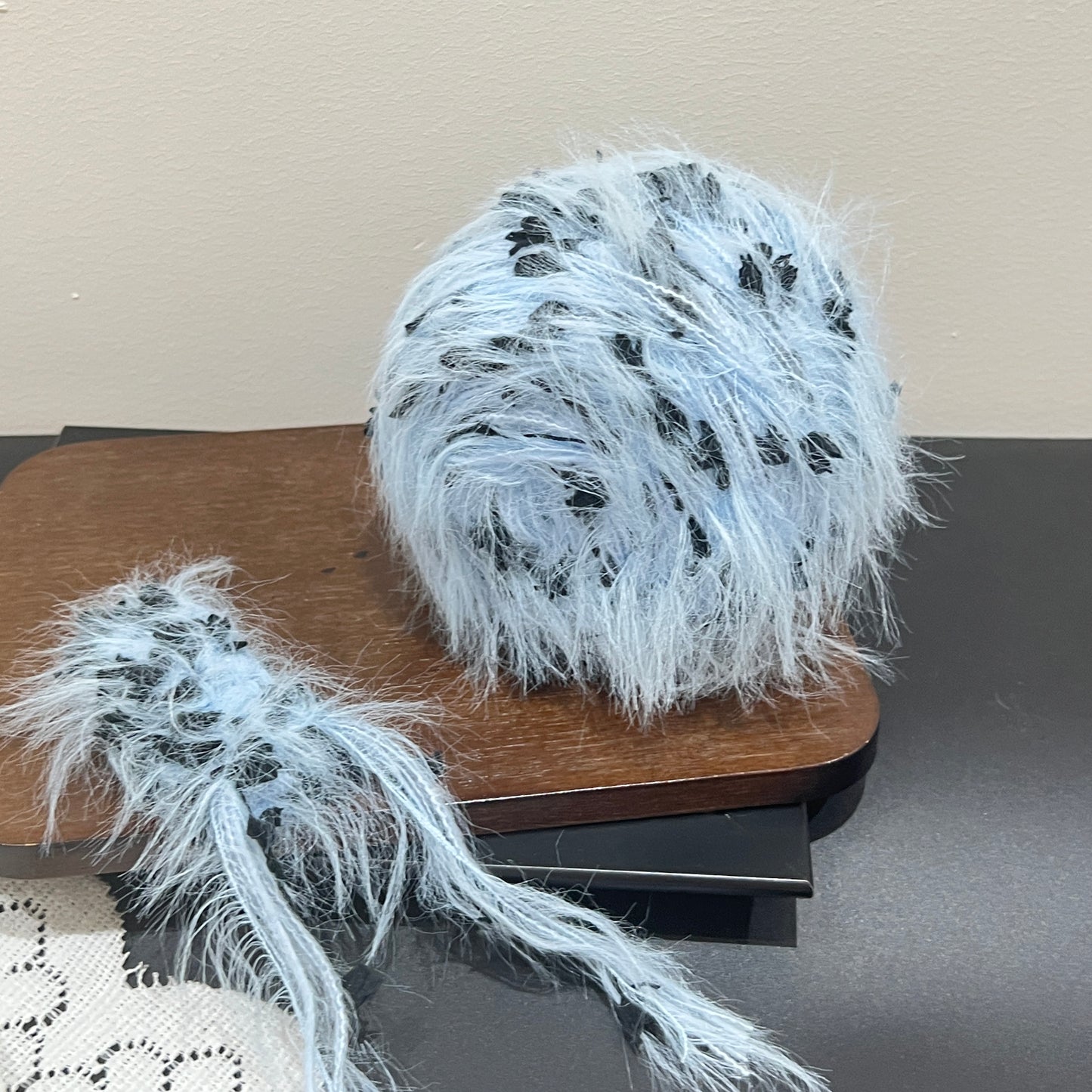 Top-down overhead center view sky black floral yarn cake, evenly distributed black petal decorative fiber fragments, fluffy long feather strands covering surface