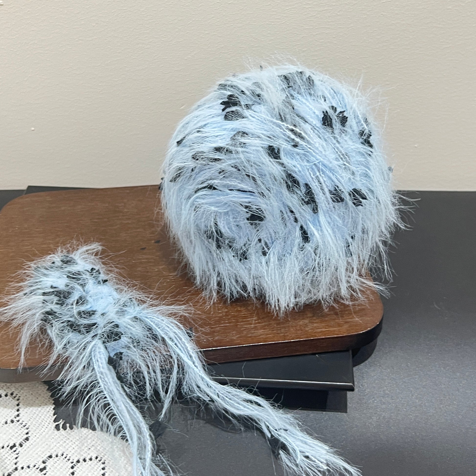 Top-down overhead center view sky black floral yarn cake, evenly distributed black petal decorative fiber fragments, fluffy long feather strands covering surface