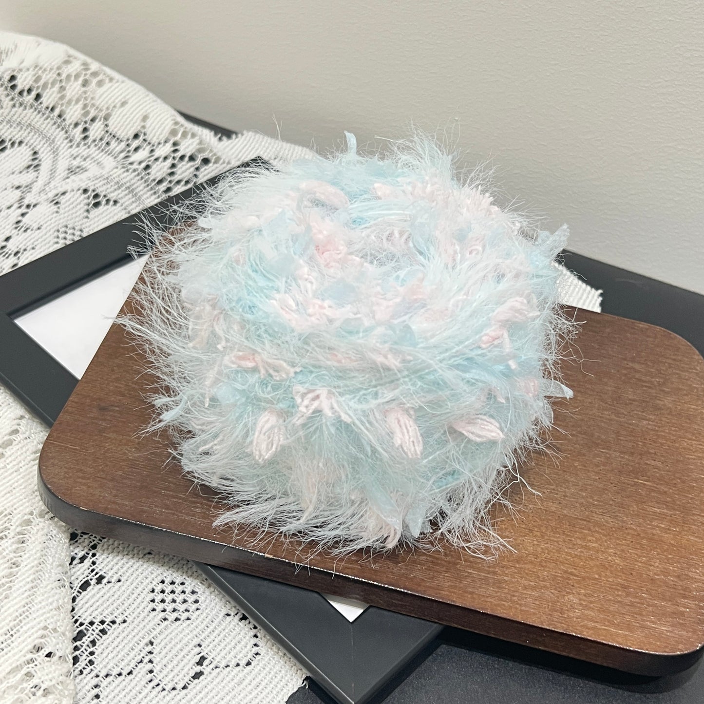 Front overhead spherical shot of pastel sky blue base hand-blended yarn cake mixed with blush pink petal fiber fragments, showing distinct airy fuzzy layered texture