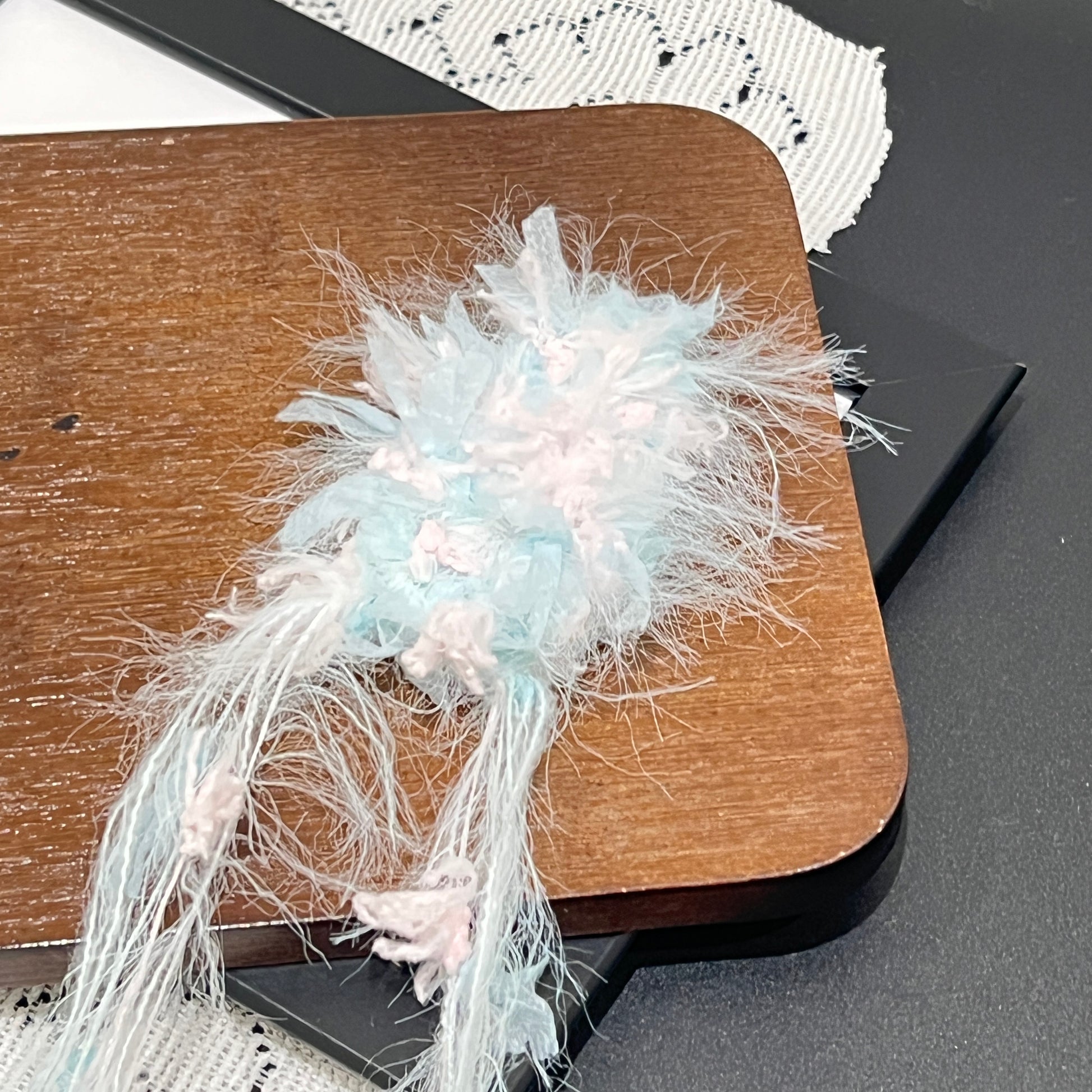 Side layout complete set: sky pink yarn cake + matching detached fiber swatch, hollow white lace fabric laid on dark matte countertop surface
