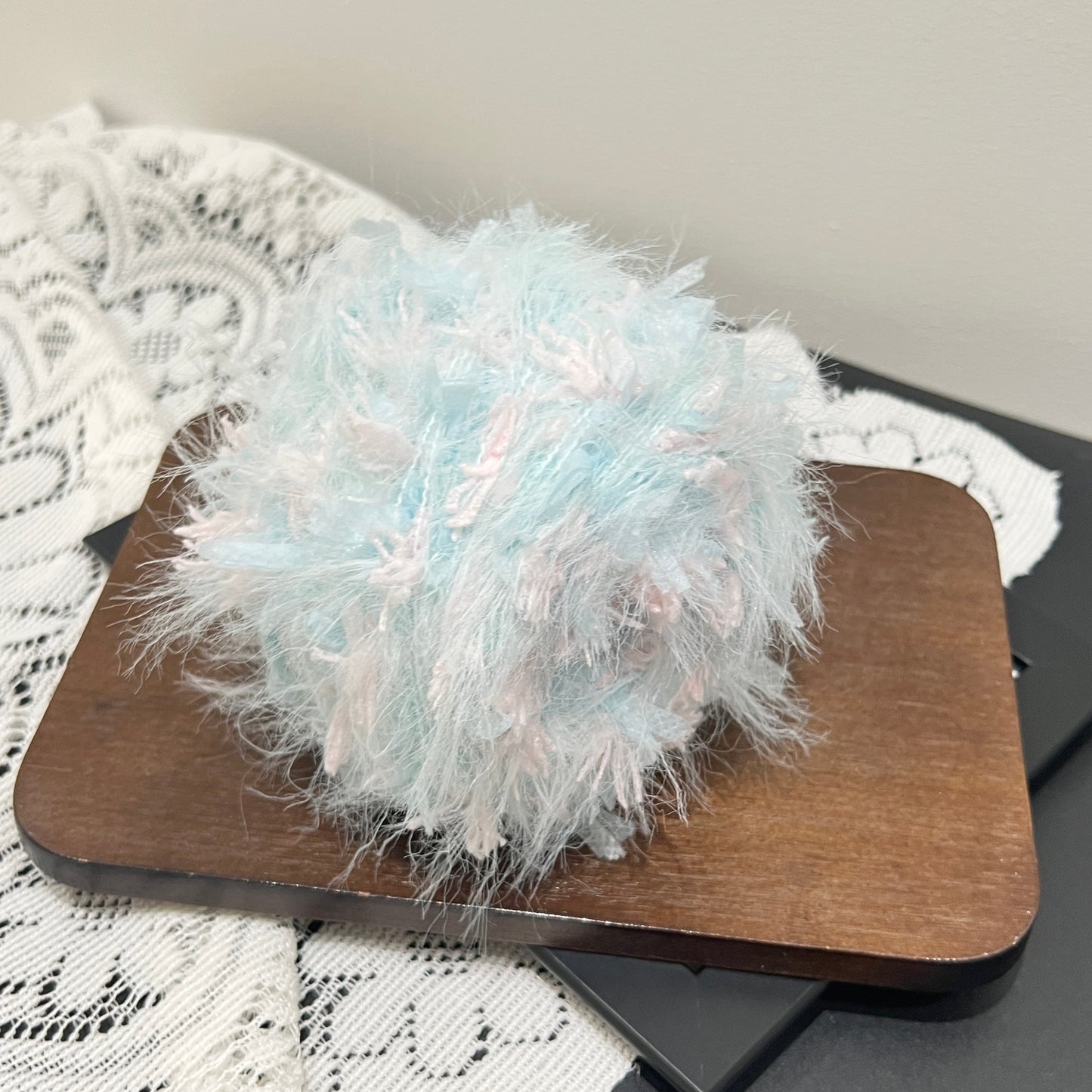 Top-down full overhead shot of sky pink blended yarn ball, showcasing multi-layer feather fluff and evenly scattered blush pink petal decorative fibers