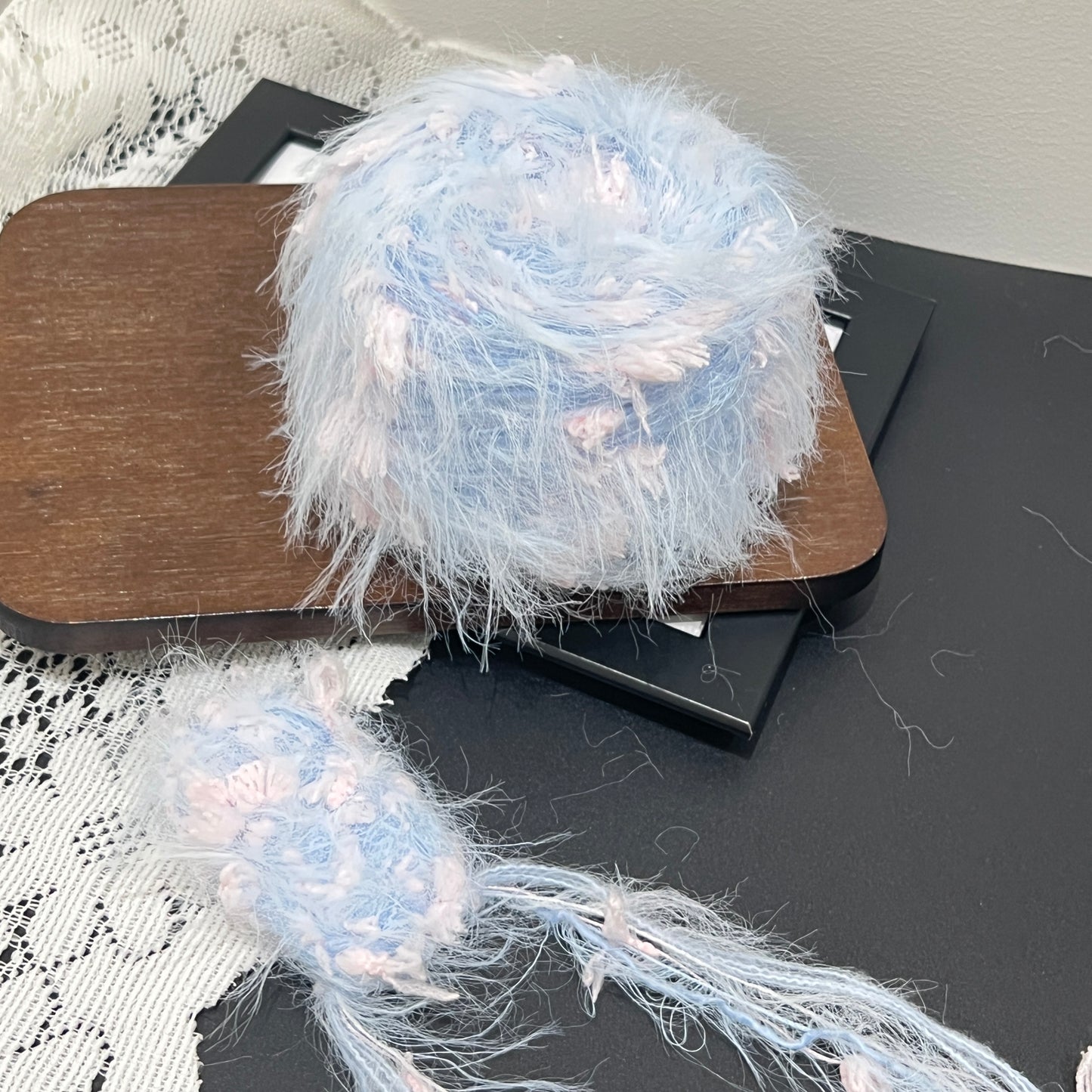 Front overhead spherical shot soft pastel sky blue base hand-blended yarn ball mixed with blush pink petal ribbon fiber fragments, airy layered feather texture