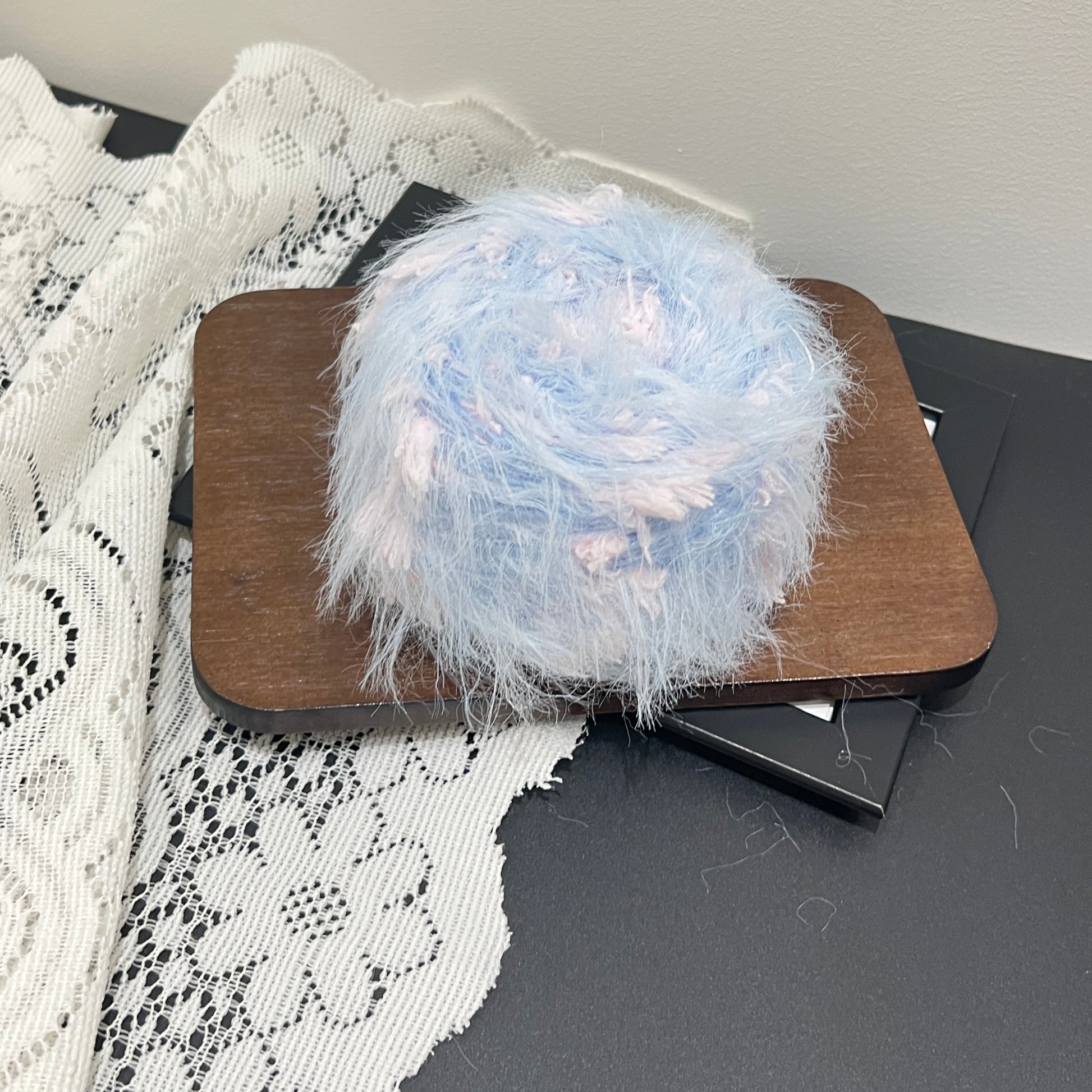 Complete display set: sky pink yarn cake + long-tassel fiber swatch, perforated white lace fabric on dark matte countertop