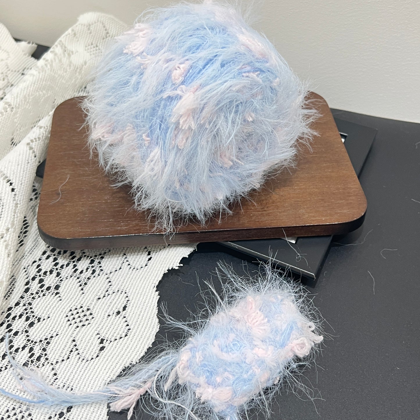 Layout shot of pastel sky blush pink floral blended yarn cake and detached fiber swatch, wooden display board, hollow white lace fabric, neutral light wall background