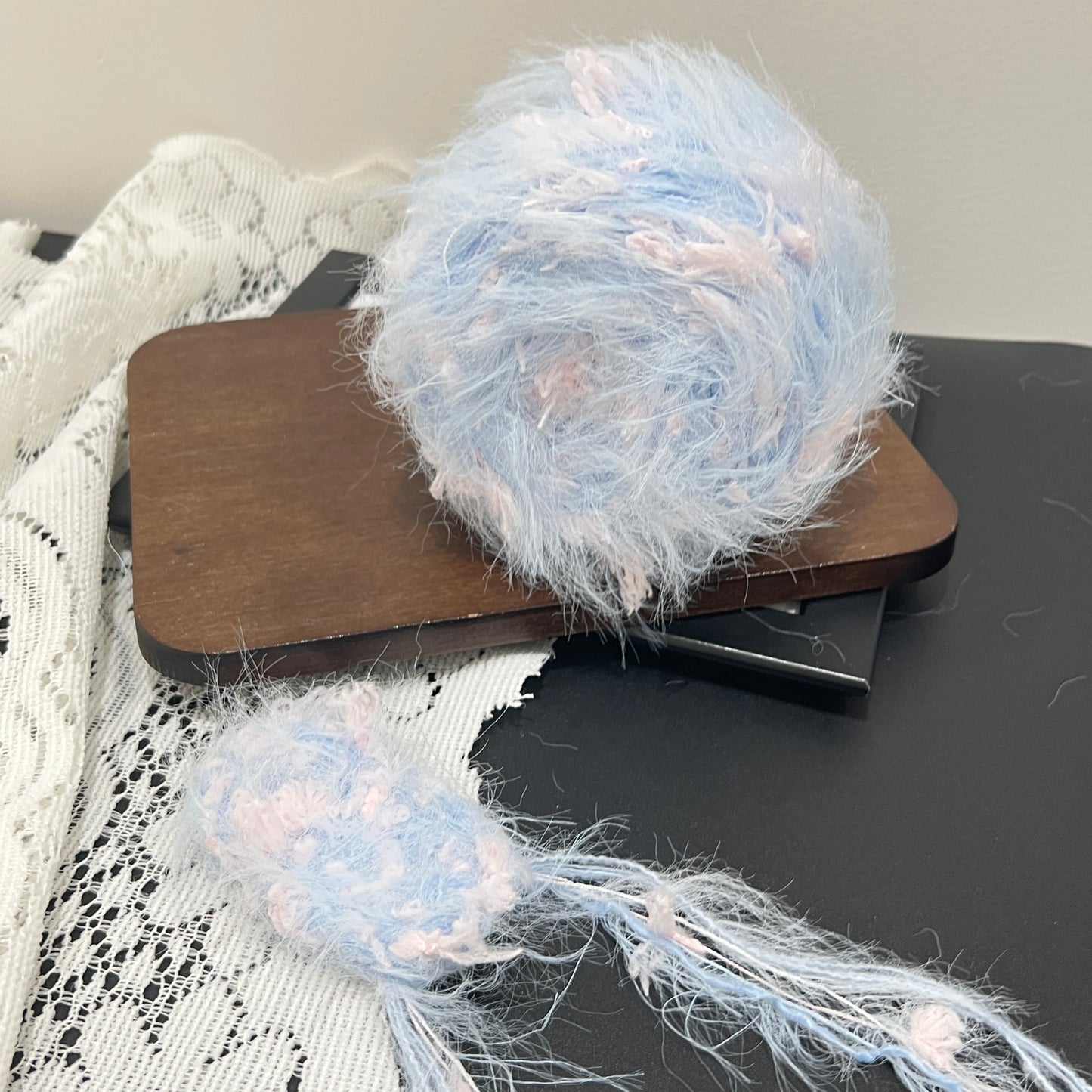 Top-down overhead center view sky pink floral yarn cake, evenly scattered blush pink petal decorative fibers, long fuzzy feather strands