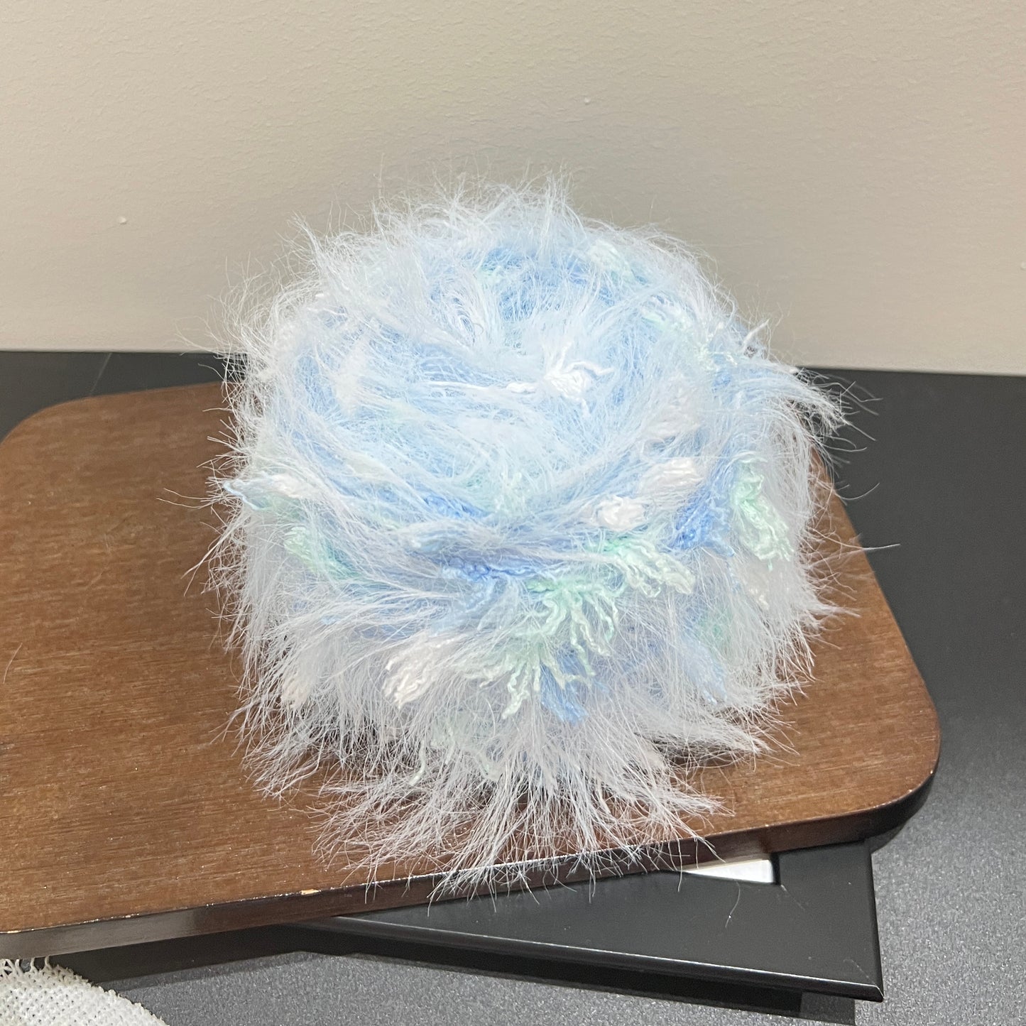 Full layout shot of sky mint yarn ball and matching fiber swatch beside hollow white lace fabric on dark countertop