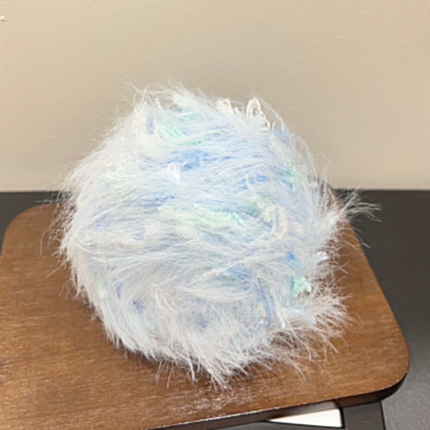 Side angle shot sky blue mint artisan blend yarn cake with scattered mint petal fiber accents