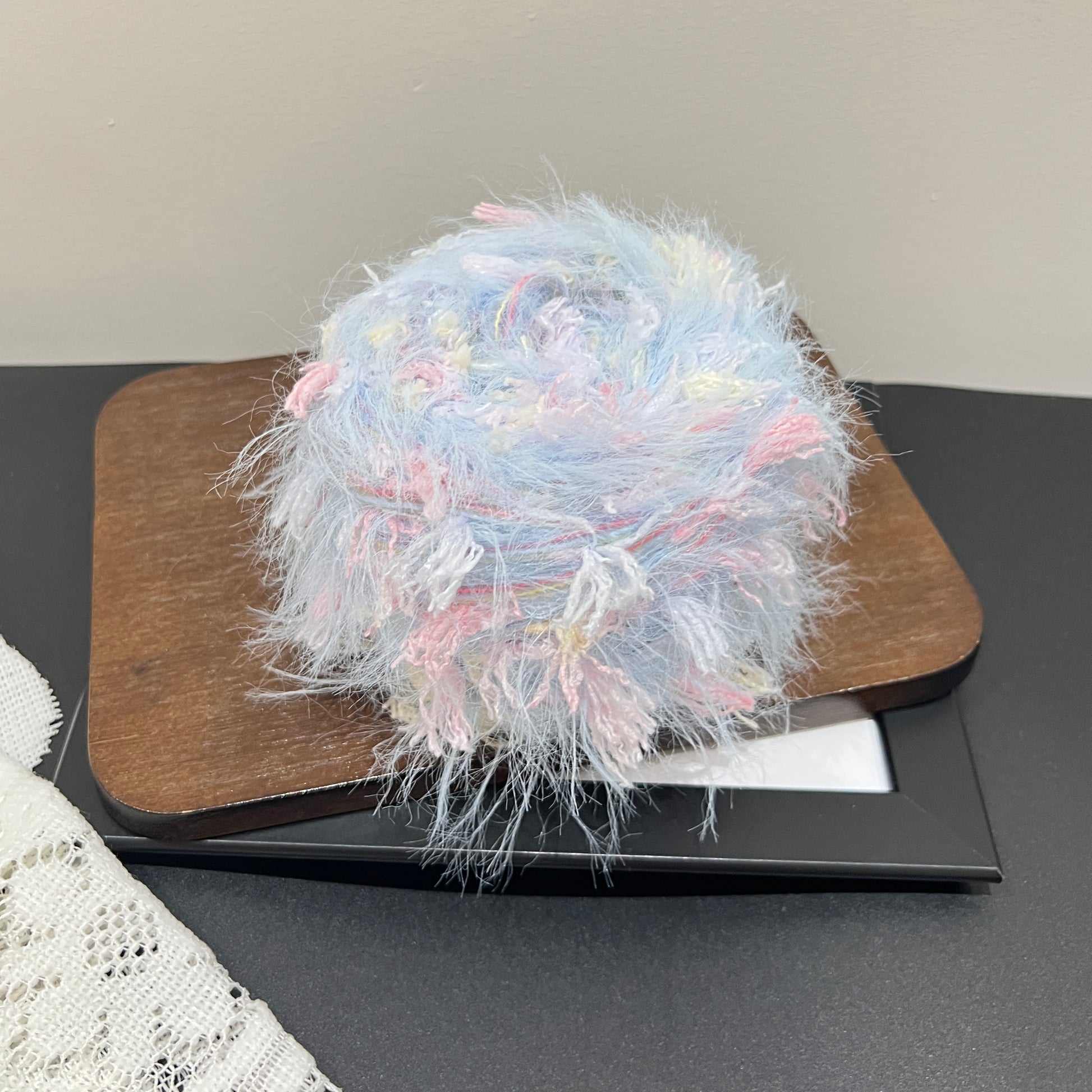 Side layout shot yarn ball + matching fiber swatch beside hollow white lace on dark countertop