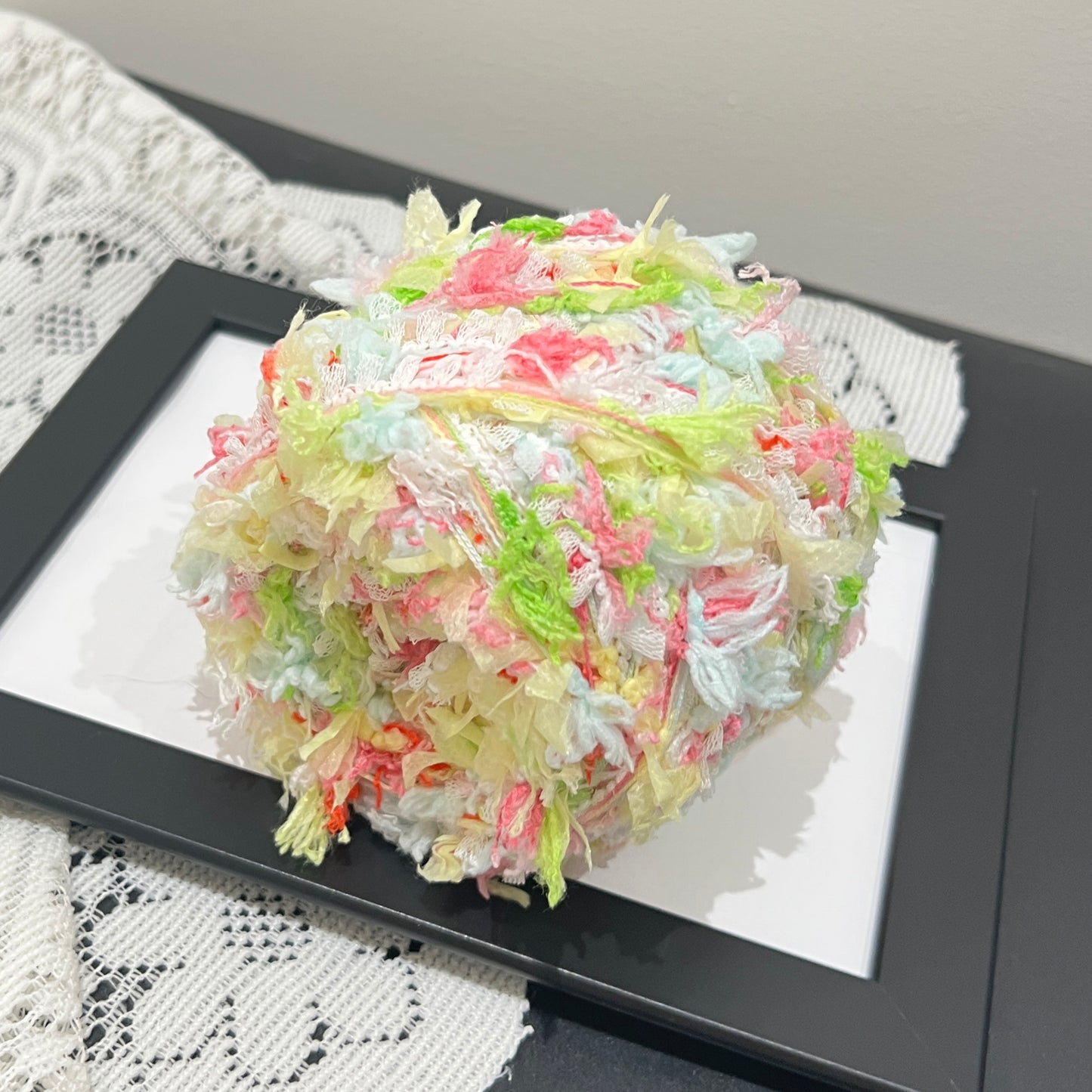Top-down overhead center view spring pastel floral yarn cake, evenly distributed multi-color shredded ribbon fiber fragments, soft layered textured surface