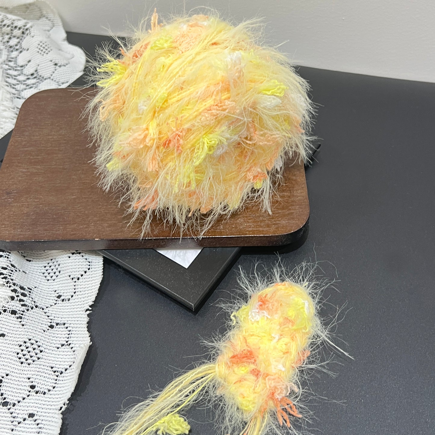 Pastel sunset yellow orange floral multi-strand hand-blended cake yarn placed on wooden display board with neutral wall backdrop