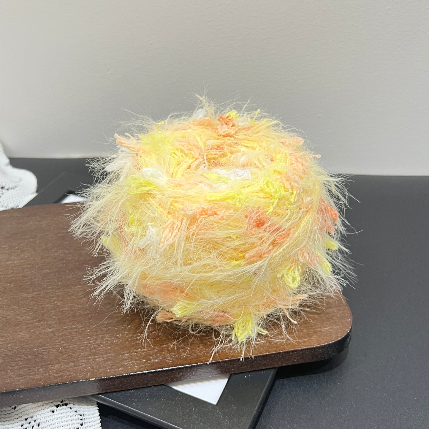Layout shot of sunset floral yarn cake and matching fiber swatch beside white lace fabric on dark countertop