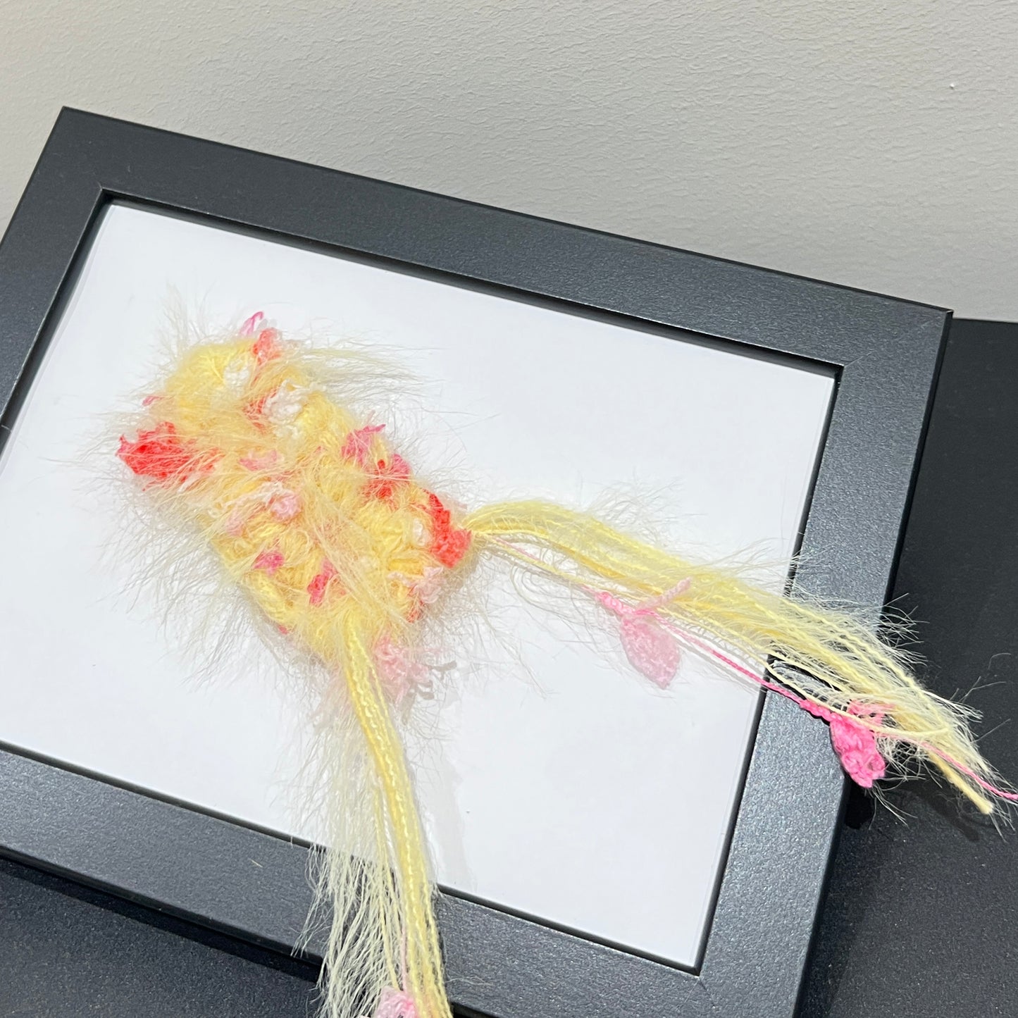 Close-up macro detail of pastel yellow blush red petal layered multi-strand blended fiber mounted on black display frame