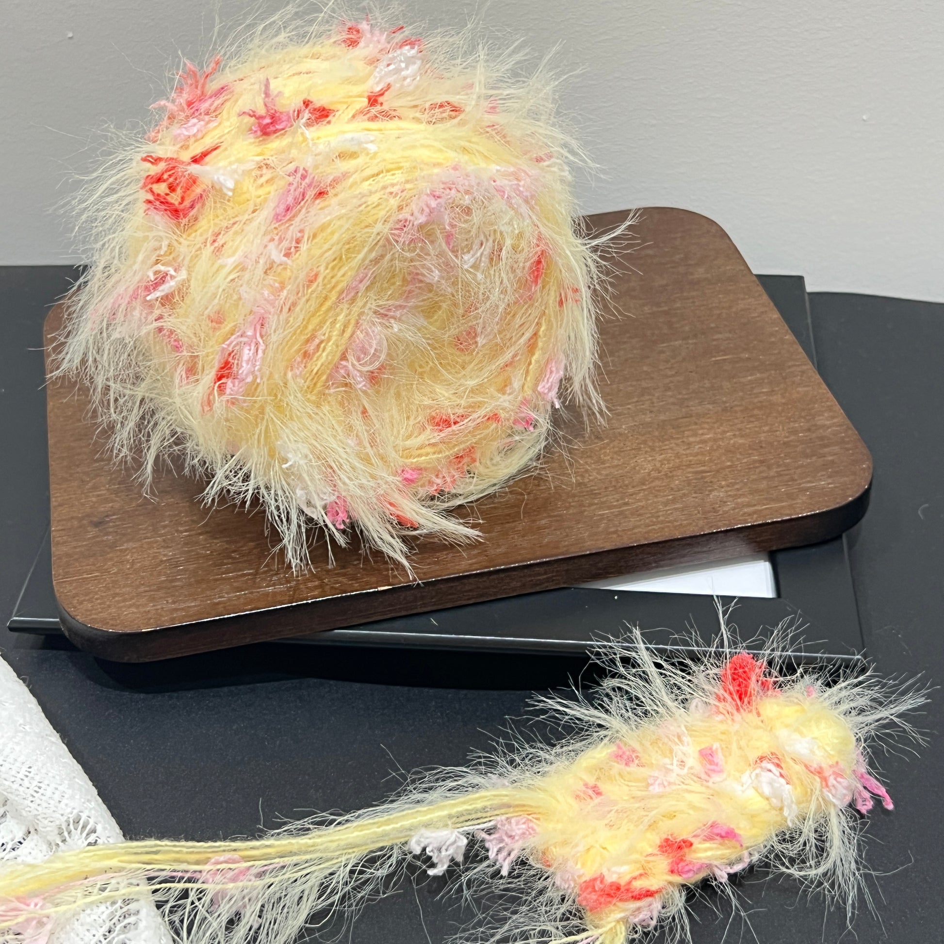 Pastel yellow blush red floral multi-strand hand-blended cake yarn placed on wooden board with dark counter backdrop