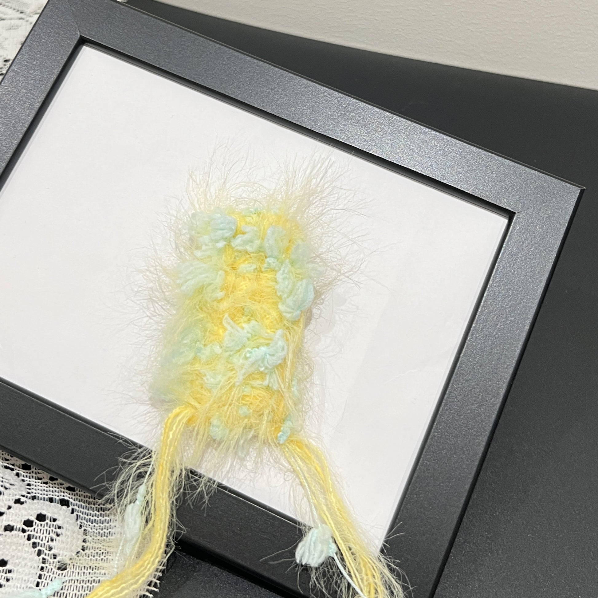 Close-up detail of pastel yellow mint petal layered multi-strand blended fiber texture on black display frame