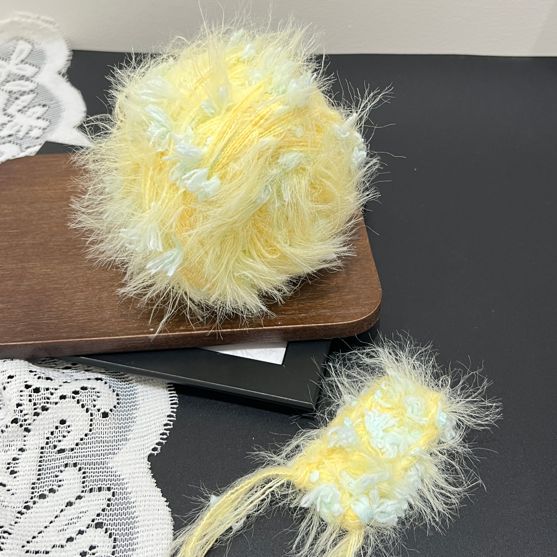 Pastel yellow mint floral multi-strand hand-blended cake yarn placed on wooden board with white lace fabric backdrop