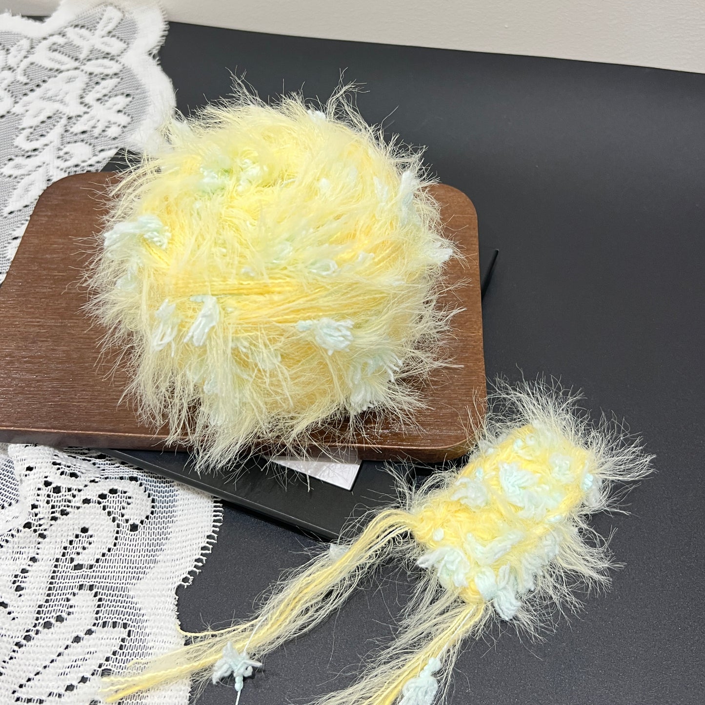Side layout pastel yellow mint floral artisan blend yarn cake and fiber sample swatch on dark countertop