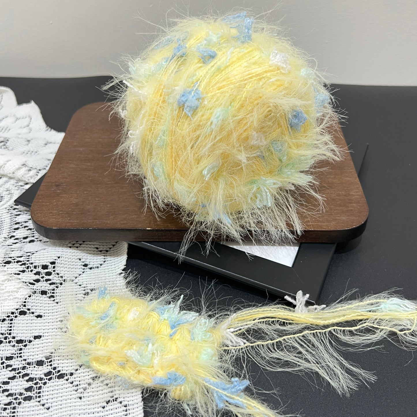Pastel yellow sky mint floral multi-strand hand-blended cake yarn placed on wooden board with hollow white lace backdrop