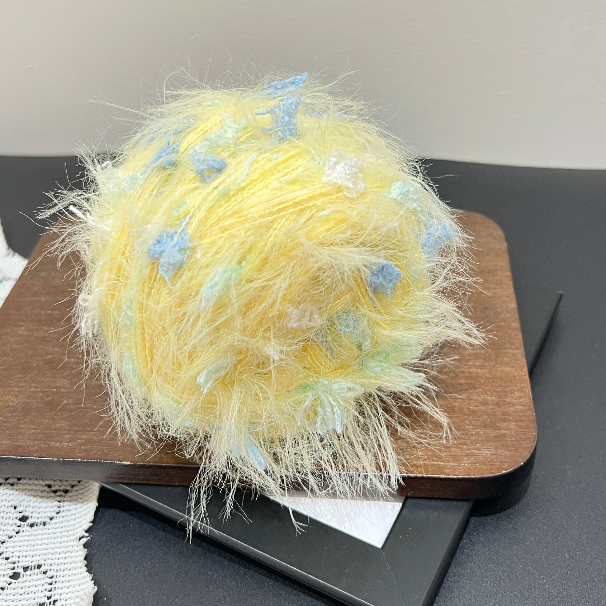 Side angle shot warm pale yellow artisan blend yarn cake scattered with sky blue and mint ribbon fiber details