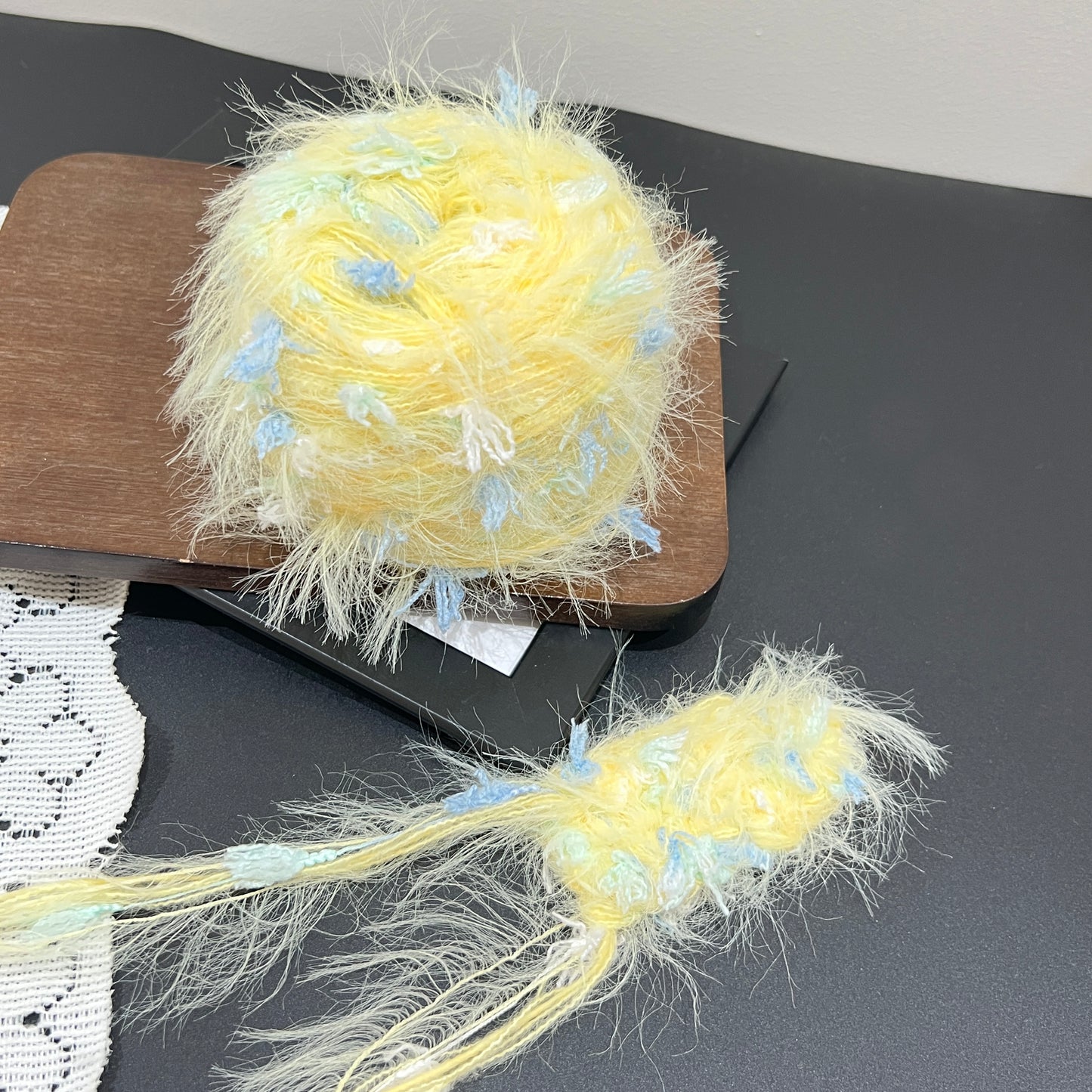 Layout shot of yellow sky mint yarn ball and matching fiber swatch beside white lace fabric on dark countertop