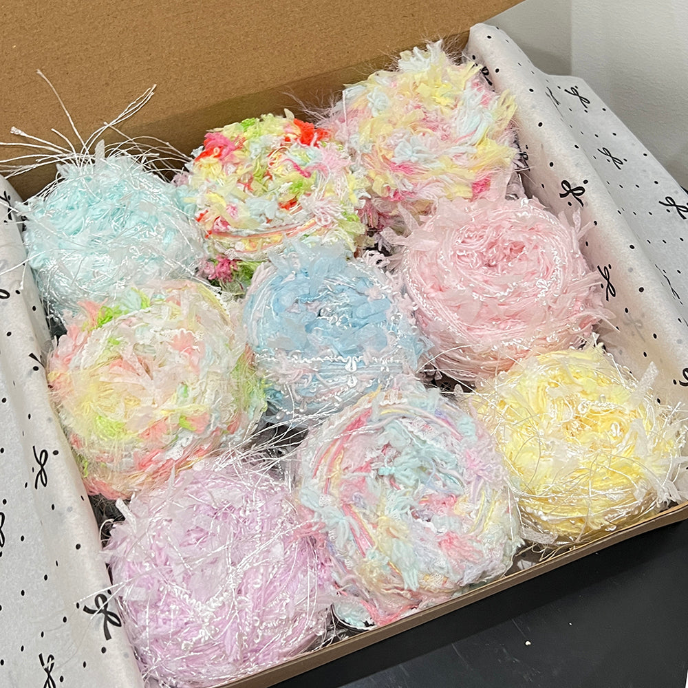 Open gift box holding 9 spring gentle floral yarn cakes, pastel yellow, mint, blush pink, lavender soft petal textured art yarn inside gift packaging