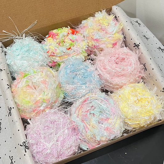 Open gift box holding 9 spring gentle floral yarn cakes, pastel yellow, mint, blush pink, lavender soft petal textured art yarn inside gift packaging
