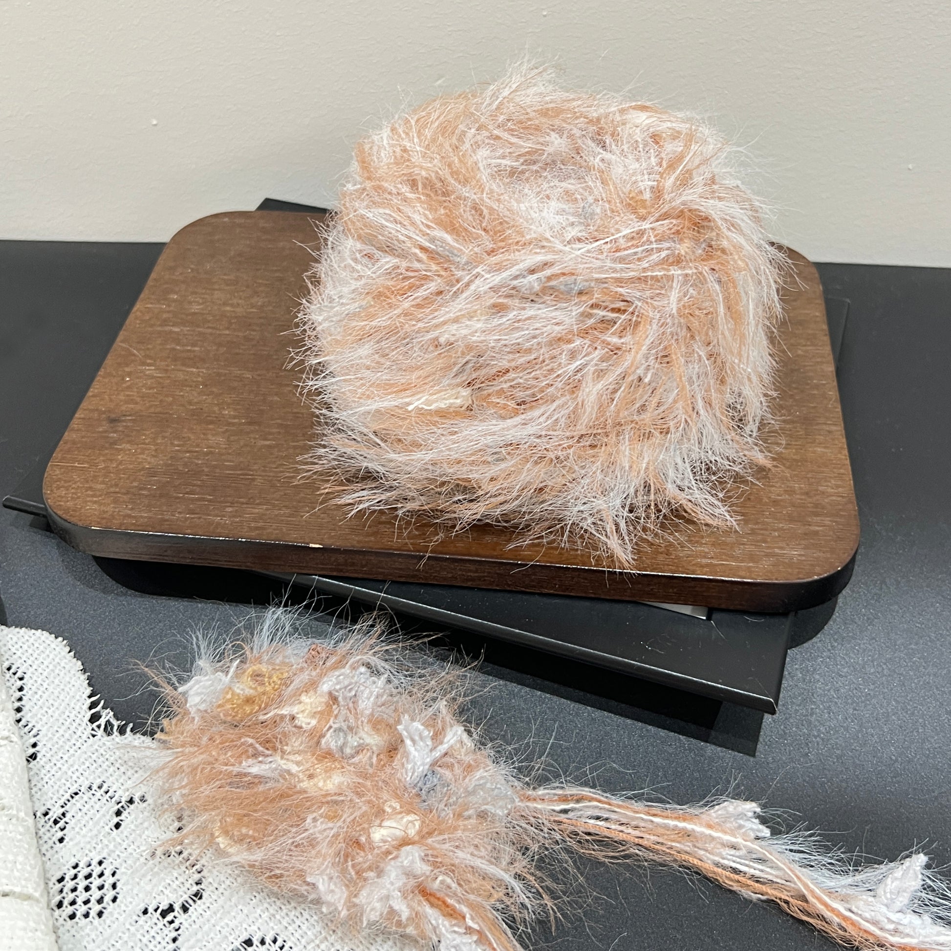 Full layout display set: caramel ivory yarn cake + detached fiber swatch, perforated white lace fabric laid on dark matte countertop