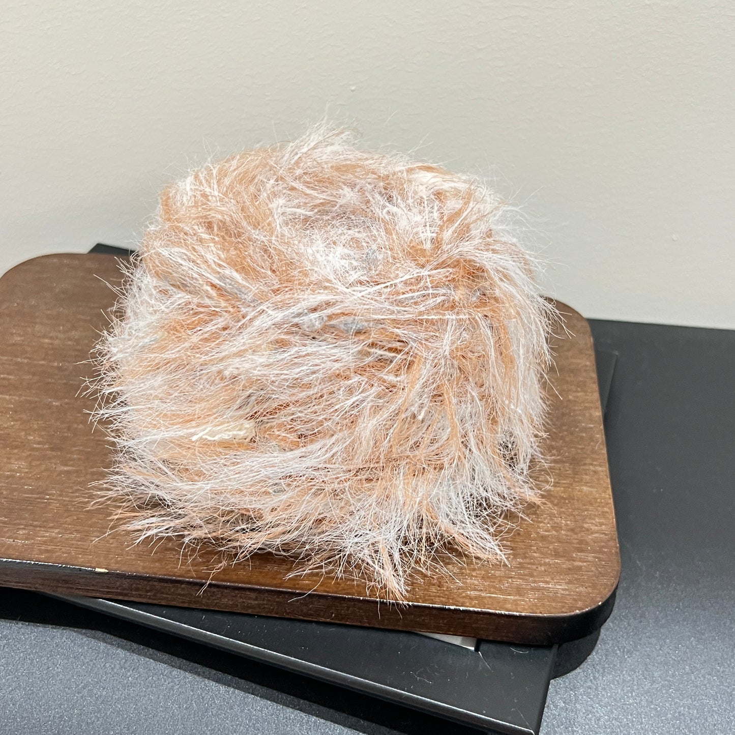 Rotated side overhead shot caramel ivory art yarn cake, layered airy feather and multi-neutral petal fiber clearly visible
