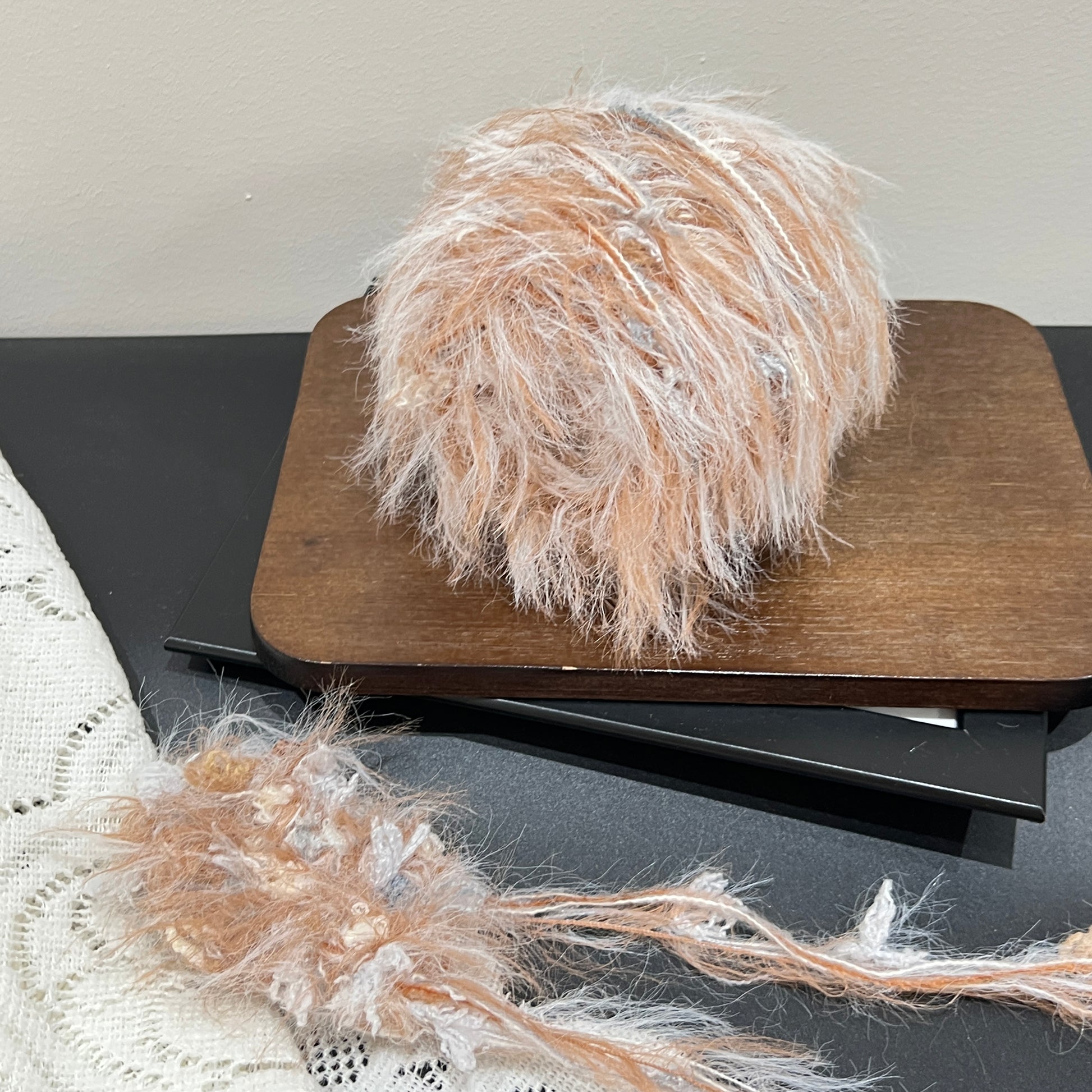 Top-down overhead center view neutral multi-tone yarn cake, evenly scattered caramel, ivory and faint gray decorative fiber pieces, fluffy feather strands