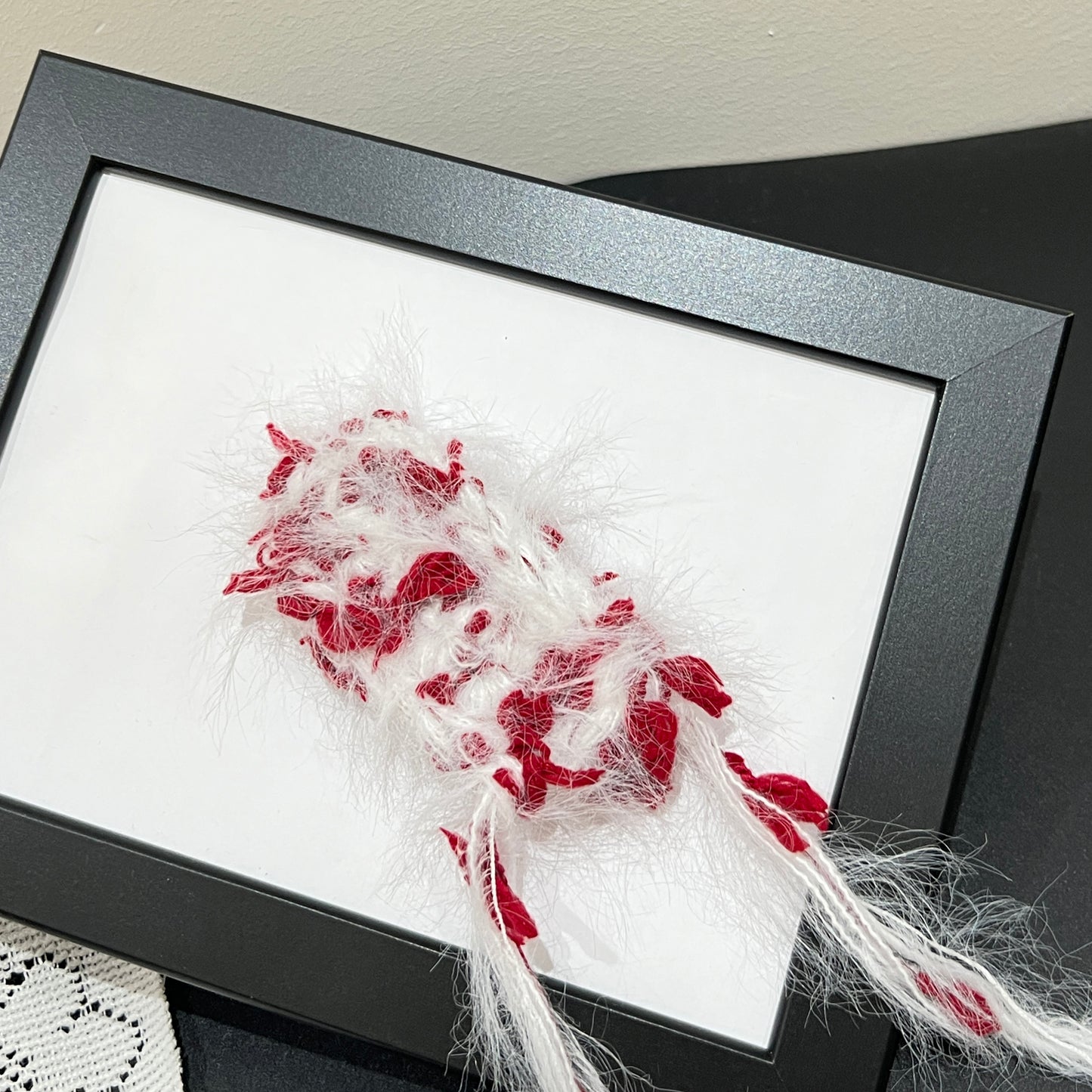 Close-up macro detail of white crimson petal layered multi-strand blended fiber mounted on black display frame