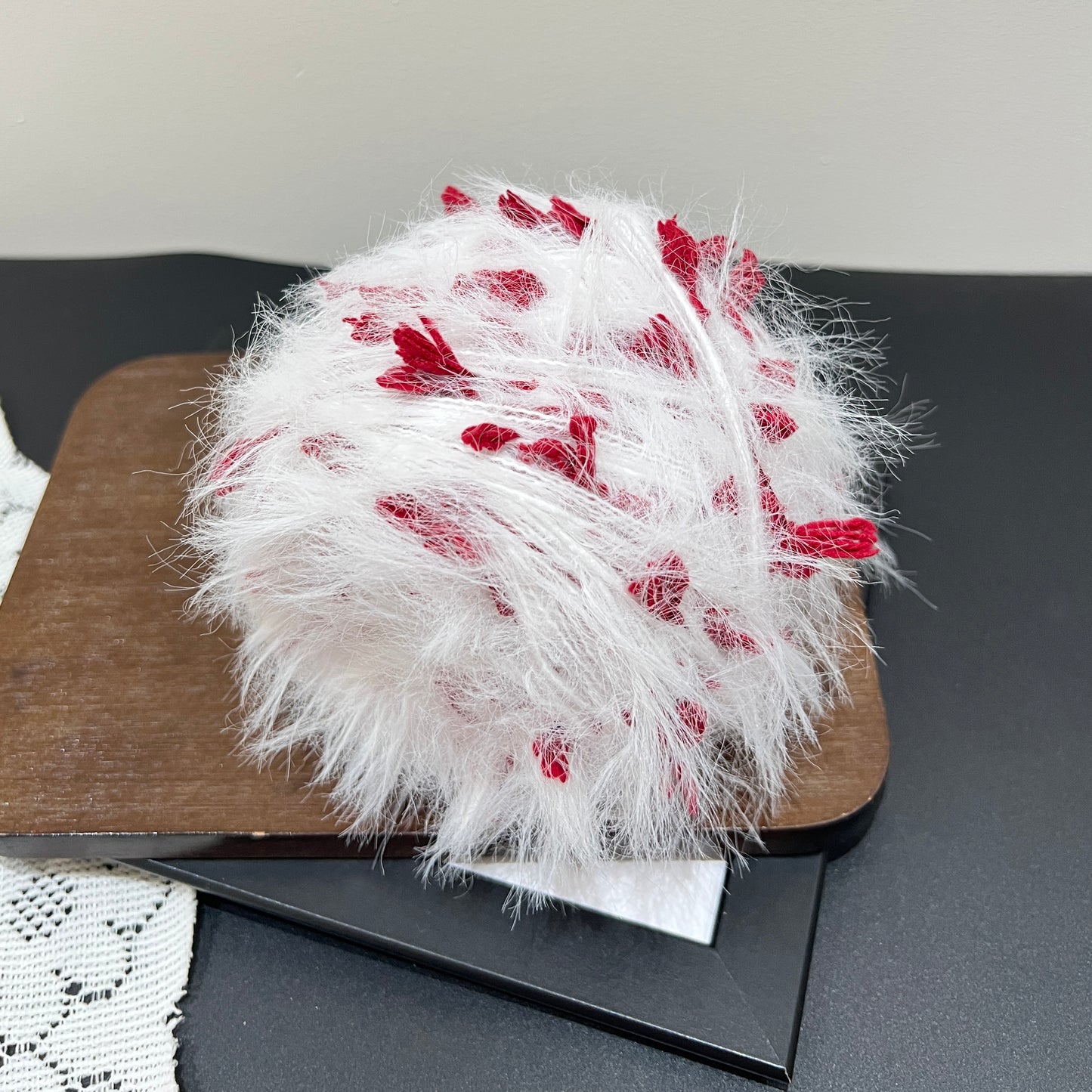 Side angle shot white base with scattered crimson petal fiber accents artisan blend yarn cake